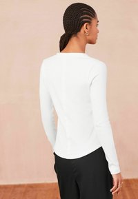 Wit langemouwtop met een getailleerd ontwerp, ronde halslijn en ribbeltextuur. In combinatie met zwarte broek, die een gladde, ronde zoom laat zien.