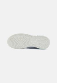 White sneaker sole with circular tread pattern, textured rubber for grip, and embossed logo detail. Made from durable materials.