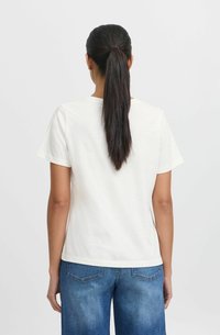 White cotton t-shirt with short sleeves, round neckline, and relaxed fit, paired with blue denim shorts displaying back pockets.