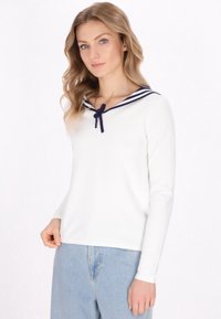 Top bianco a maniche lunghe con colletto da marinaretto, decorato con strisce navy e un fiocco, abbinato a pantaloni in denim azzurro chiaro.