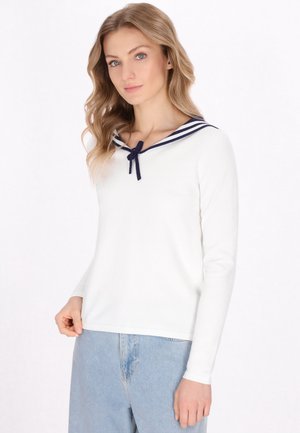 Top bianco a maniche lunghe con colletto da marinaretto, decorato con strisce navy e un fiocco, abbinato a pantaloni in denim azzurro chiaro.