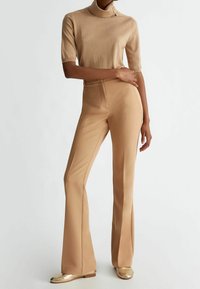 Beige gebreide coltrui met korte mouwen, met knoopdetail. Uitlopende beige broek met een gladde textuur en een aansluitende taille.