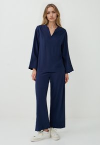 Marineblauw twee-delige outfit met een trui met V-hals en brede mouwen, gecombineerd met loszittende broek gemaakt van zachte stof.
