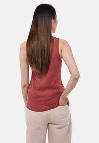 Débardeur côtelé bordeaux avec un ourlet arrondi et de larges bretelles, porté avec un pantalon beige clair comportant des poches arrière.