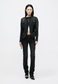 Mustast nahast mootorratturi jope, millel on lühenenud disain, lukuga esiosa ja kaks rinnakotti, koos kõrge vöökohaga mustade teksade ja terava ninaga kontsakingadega.