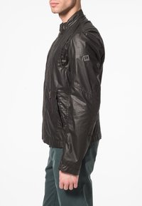 Svart, lätt bomberjacka med dragkedja framtill, sidofickor och ribbade muddar. Har en subtil glans och en logga på vänster axel.