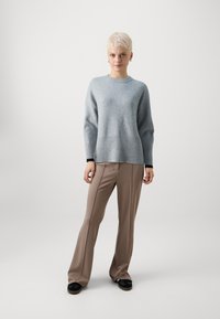 Hellgrauer Pullover mit geripptem Saum, kombiniert mit beigen Schlaghosen und schwarzen Schuhen. Weiche Textur und lässige Passform.