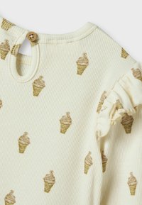 Ribbed cream fabric top featuring small brown ice cream cone patterns, round neck with a button closure, and ruffled sleeve accents.