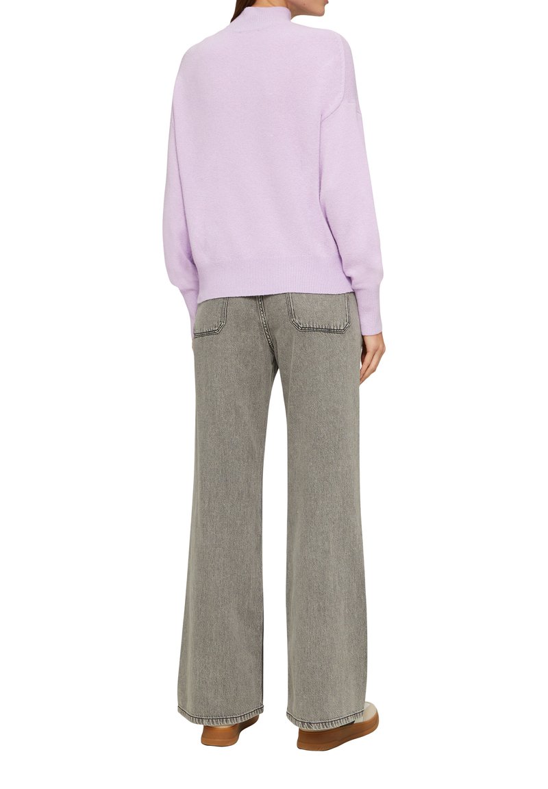 Lavendelfarbenes, leichtes Sweatshirt mit hohem Kragen, kombiniert mit grauen, hoch taillierten Schlagjeans und braunen Slippern.