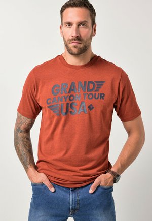 Červené tričko s melírováním a výrazným černým nápisem "TOUR GRAND CANYON USA" a stylizovanými křídly. Krátké rukávy a design s kulatým výstřihem.
