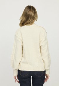 Pull en tricot texturé ivoire avec des détails en maille torsadée, ourlet et poignets côtelés, doté d'un col rond et d'une coupe ample.