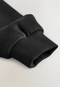 Mustad pikad varrukad mansetiga, millel on soonikuga kootud tekstuur ja elastne kogumine lihtsal heledal taustal.