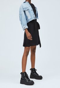 Denimkort jacka med knäppningar, svart klänning med bälte i midjan, och texturerade svarta kängor med kraftiga sulor.