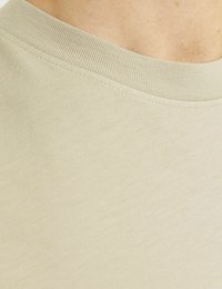 Light beige short-sleeve shirt with a ribbed crew neckline. Smooth fabric texture with minimal stitching details.