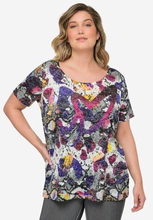 Haut à manches courtes coloré présentant un motif multicolore en violet, rose et jaune sur fond blanc, avec une coupe décontractée et un décolleté arrondi.