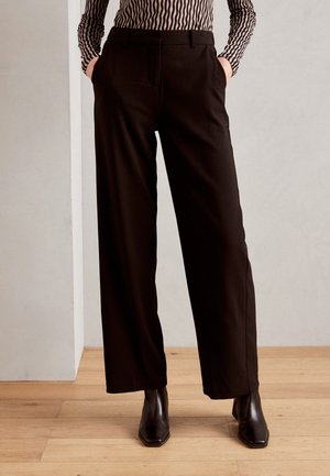 Zwarte, wijde broek met frontzakken. Zachte stof, op maat gemaakte pasvorm en een gladde textuur. Gecombineerd met zwarte, vierkante enkellaarsjes.