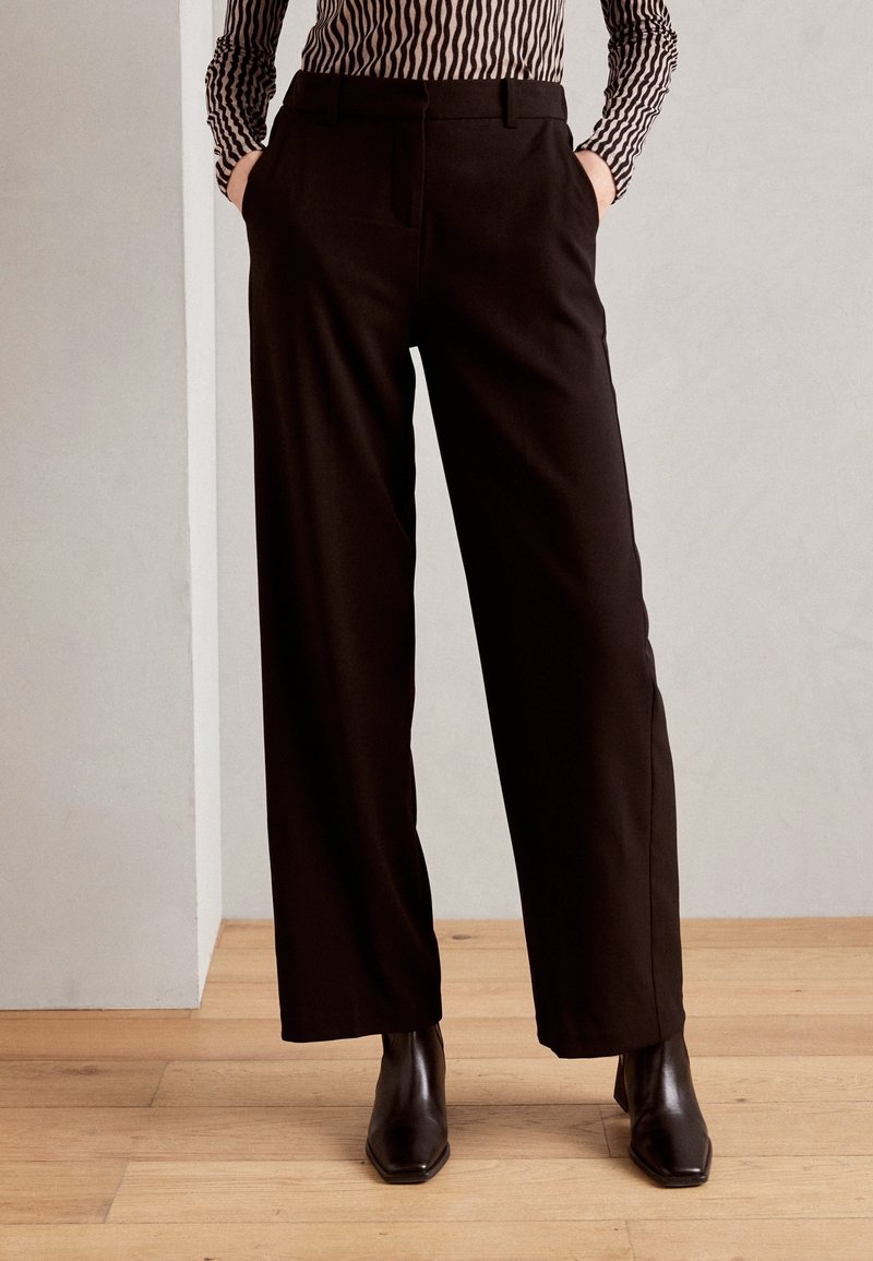 Svarta, vida byxor med framfickor. Mjuk tyg, skräddarsydd passform och en slät struktur. Matchas med svarta, fyrkantiga ankelstövlar.