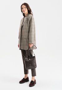 Szary w kratę blazer na białej bluzce, brązowa skórzana torba worek, brązowe spodnie o teksturowanej powierzchni oraz bordowe mokasyny z detalem w postaci hardware.