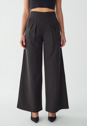Brede, hoge, op de taille zittende broek in donkere stof met plooien, effen kleur, gladde textuur en een nette afwerking. Gepaard met puntige schoenen.