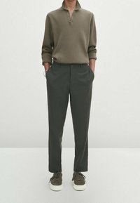 Oliwkowa zielona koszulka polo z długim rękawem i kołnierzykiem, zestawiona z ciemnoszarymi spodniami i brązowymi trampkami z białymi podeszwami. Prosty design i krój.