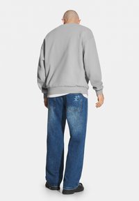 Szary sweter z długimi rękawami i ściągaczami, zestawiony z luźnymi, ciemnoniebieskimi dżinsami o jasnym wykończeniu i detalach przy tylnej kieszeni.