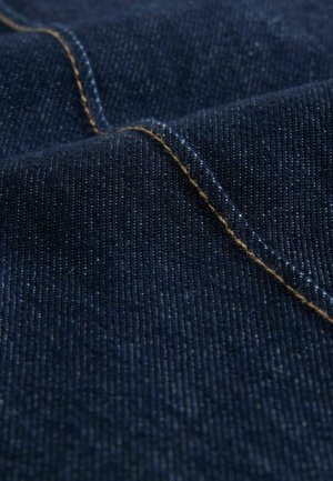 Denim fabric in deep blue with a smooth texture, featuring golden-yellow stitching along one seam, showcasing its woven pattern.
