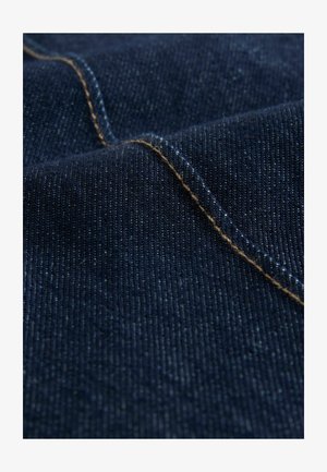 Denimstof in diepblauw met een gladde textuur, met goudgele stiksels langs één naad, die het geweven patroon benadrukt.