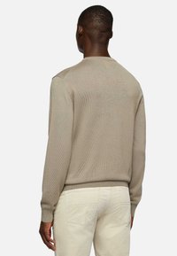 Beige knit sweater with a round neckline, ribbed cuffs, and hem. Features a textured finish and a fitted silhouette, worn with cream pants.
