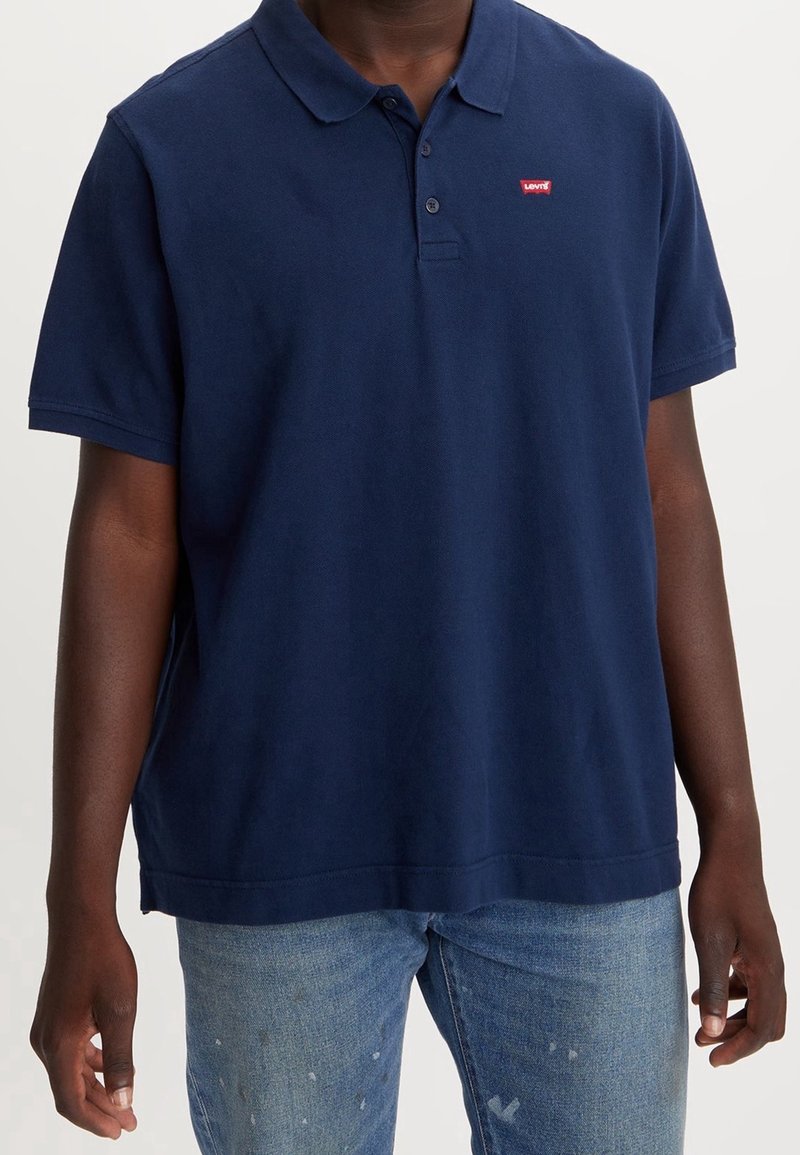 Marinblå polo skjorta, ribbat krage, korta ärmar, fem-knappsstängning, med en liten röd Levi's-logotyp på vänster bröst, i bomullsmaterial.