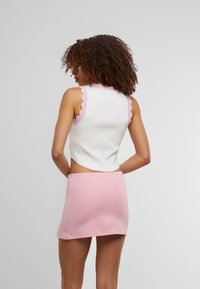 Top court blanc avec des bords festonnés roses, associé à une jupe courte rose. Le tissu semble lisse et ajusté, mettant en avant un design minimaliste.