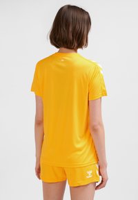 Gul sporttröja med rund hals, korta ärmar och vita detaljer på axlarna. Matchas med matchande shorts med en logotyp.