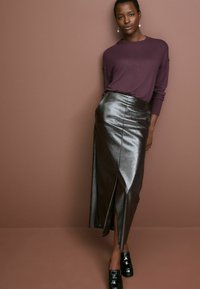 Maglione viola scuro a maniche lunghe abbinato a una gonna maxi in pelle nera con uno spacco laterale. Mocassini neri completano l'outfit.