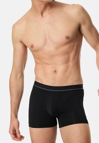 Schwarze Boxer-Shorts aus weichem Material, mit einer körpernahen Passform, elastischem Bund mit einem weißen Akzent und einer glatten Oberfläche.