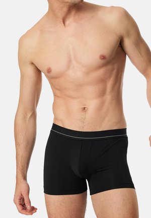 Schwarze Boxer-Shorts aus weichem Material, mit einer körpernahen Passform, elastischem Bund mit einem weißen Akzent und einer glatten Oberfläche.
