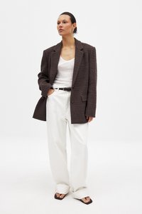 Brauner Blazer mit Struktur, weißes Tanktop, weiße weitgeschnittene Hose und braune Absatzsandalen. Der Blazer hat große Revers und einen Einzelknopfverschluss.