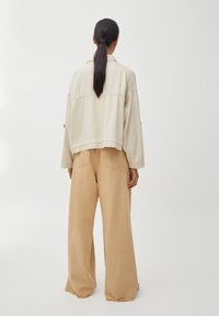 Veste oversize crème avec un col et des poignets boutonnés associée à un pantalon beige ample, doté d'une taille haute et de poches latérales.