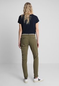 Olivgröna chinos med smal passform, detaljerade bakfickor och ett vävt bälte. Matchas med en kortärmad marinblå topp och vita sneakers.