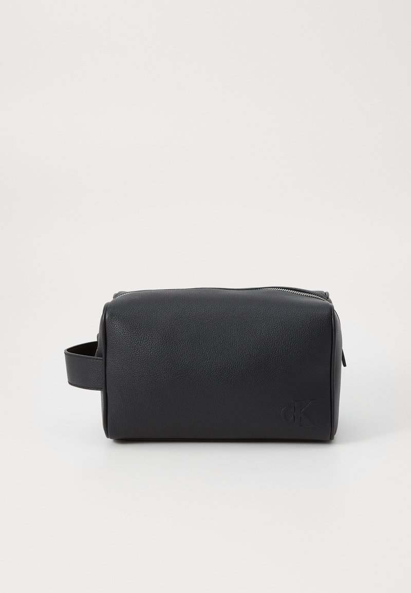 Schwarze Kosmetiktasche aus Leder mit zylindrischer Form, Reißverschluss und einem seitlichen Griff. Mit geprägtem Logo-Detail auf einer Seite.