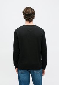 Black long-sleeve t-shirt with a round neckline, smooth fabric texture, and a simple design, paired with blue jeans.