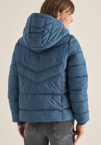 Giacca puffer blu isolata con cappuccio, caratterizzata da cuciture a chevron, un motivo trapuntato orizzontale e polsini elasticizzati per mantenere il calore.