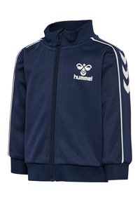 Veste zippée marine en tissu lisse, présentant un col haut, un logo Hummel sur la poitrine et des rayures blanches le long des épaules.