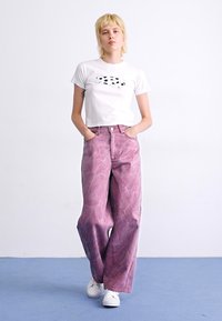T-shirt cropped blanc avec un design abstrait noir, assorti à un jean rose marbré taille haute et à jambes larges, et des baskets blanches.