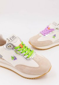 Sneakers med beige mocka och vitt syntetiskt överdel, med lila och gröna snören, silverdetaljer och triangulära lila och gröna detaljer.