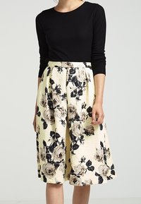 Maglietta nera a coste con maniche lunghe abbinata a una gonna gialla al ginocchio con motivi floreali neri e beige e un tessuto testurizzato.