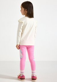 Lys cremet langærmet skjorte med flæseærmer, kombineret med pink leggings med sommerfuglemønstre. Stribede, farverige sokker og pink sko.