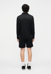 Camisa negra de manga larga con cuello, combinada con pantalones cortos negros. Tela lisa, diseño sencillo y sin patrones visibles ni detalles metálicos.