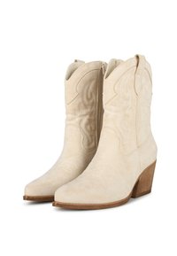 Botas de cowboy de ante beige con cremalleras laterales, puntera puntiaguda y detalles bordados. Presentan un tacón de madera apilado para mayor altura.