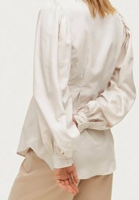 Ljusrosa silkblus med puffärmar, knappade manschetter och en avslappnad passform, med subtila plisseringar vid axlarna och bakseam.