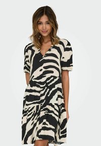 Robe en imprimé zèbre noir et crème avec un col en V, des manches courtes et un design à volants. Fabriquée en tissu léger avec une silhouette fluide.