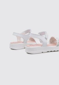 Sandalias blancas con suela de goma texturizada, diseños recortados y correa ajustable en el tobillo. Plantilla suave de color rosa para mayor comodidad.